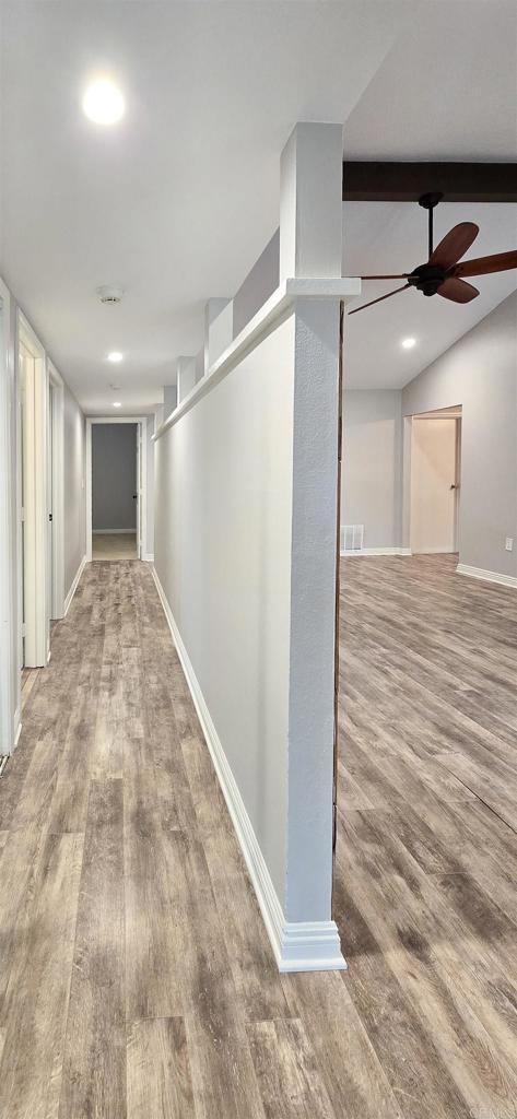 hallway with visible vents, baseboards, wood finished floors, and vaulted ceiling with beams