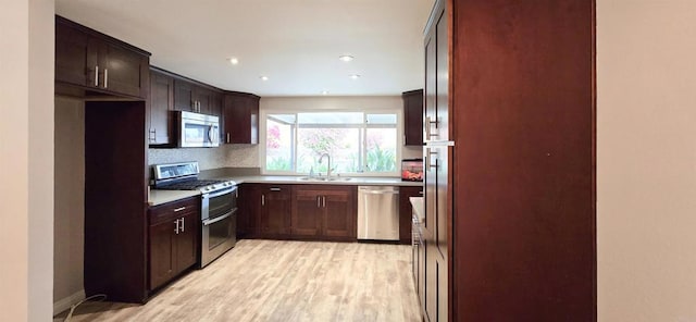 kitchen featuring light wood-style flooring, a sink, stainless steel appliances, dark brown cabinetry, and light countertops