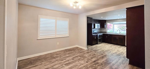 kitchen featuring baseboards, light wood-style flooring, a sink, dark brown cabinets, and appliances with stainless steel finishes