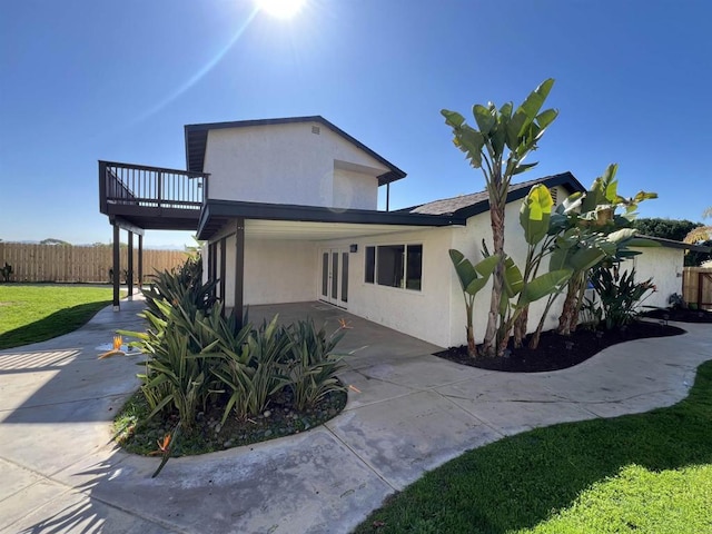 view of property exterior featuring a patio, a balcony, fence, stucco siding, and a lawn