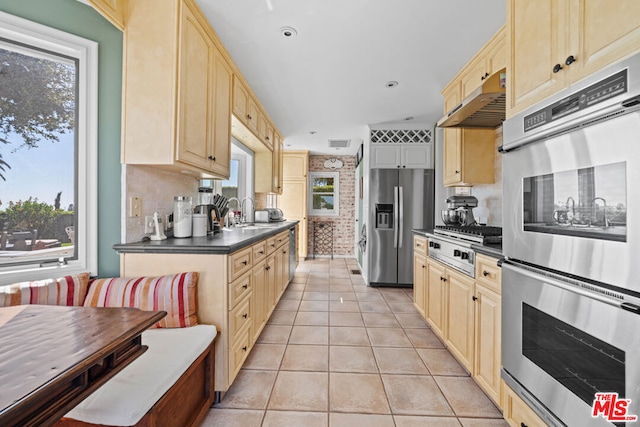 kitchen with light tile patterned floors, light brown cabinetry, stainless steel appliances, breakfast area, and decorative backsplash