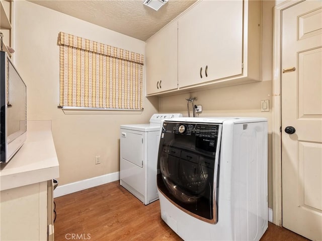 laundry room with cabinets, washing machine and dryer, a textured ceiling, and light hardwood / wood-style flooring