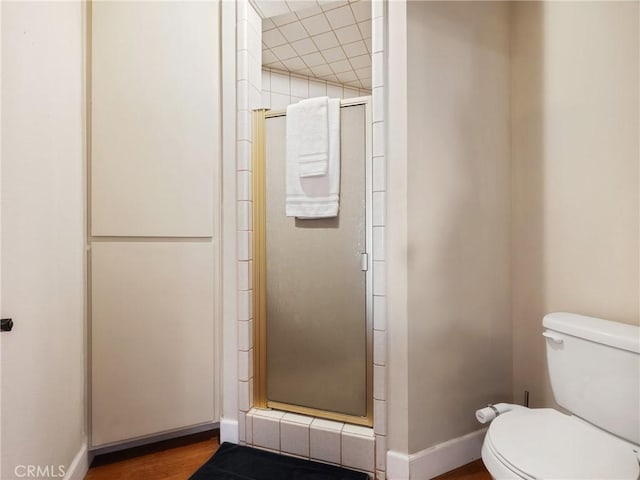 bathroom with hardwood / wood-style flooring, a shower with shower door, and toilet