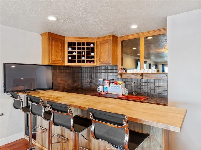 kitchen featuring tasteful backsplash, butcher block countertops, a kitchen breakfast bar, and sink