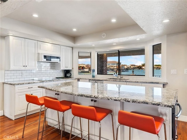 kitchen featuring light stone countertops, a water view, a center island, and white cabinets