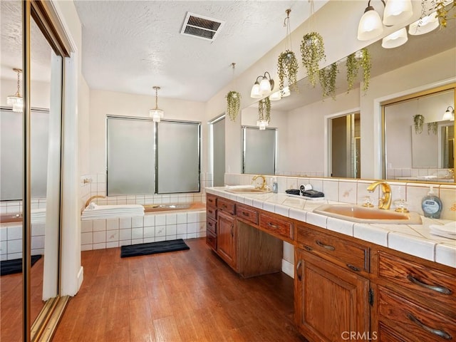 bathroom with wood-type flooring, a textured ceiling, vanity, and tiled tub