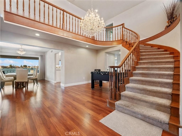 stairs with an inviting chandelier, a towering ceiling, and hardwood / wood-style floors