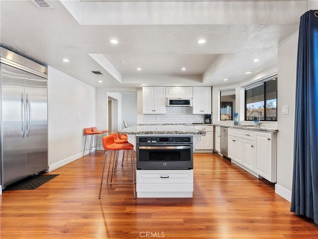 kitchen featuring appliances with stainless steel finishes, white cabinetry, light stone counters, a kitchen island, and a raised ceiling