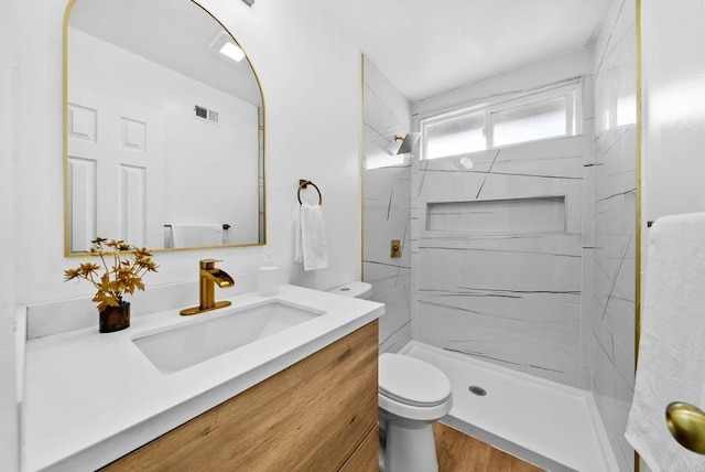 bathroom with tiled shower, vanity, and toilet