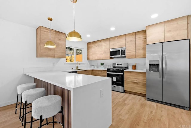 kitchen featuring sink, a kitchen bar, hanging light fixtures, stainless steel appliances, and light hardwood / wood-style flooring