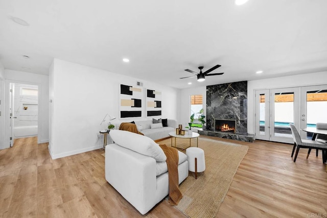 living room with light hardwood / wood-style floors, a premium fireplace, ceiling fan, and french doors