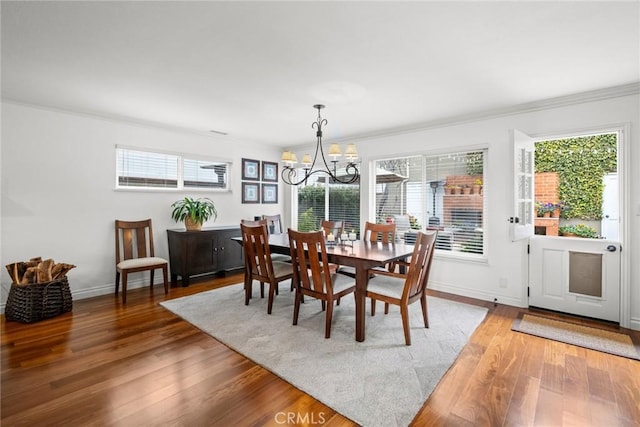 dining room with a healthy amount of sunlight, wood finished floors, ornamental molding, and an inviting chandelier