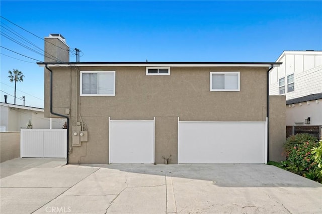 rear view of house featuring stucco siding, driveway, fence, an attached garage, and a chimney