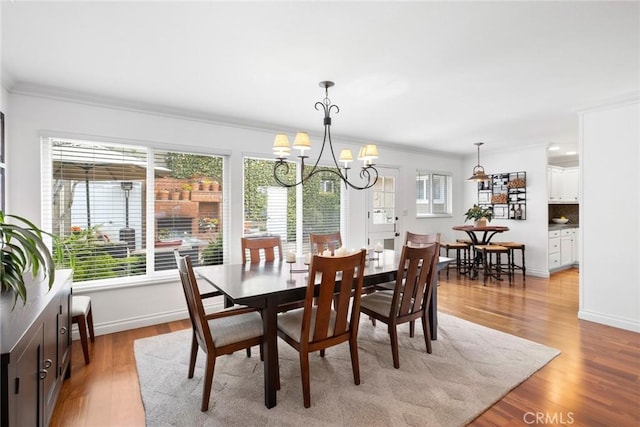 dining area with light wood-type flooring, baseboards, an inviting chandelier, and crown molding