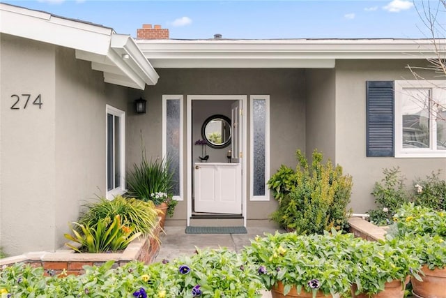 entrance to property featuring a chimney and stucco siding