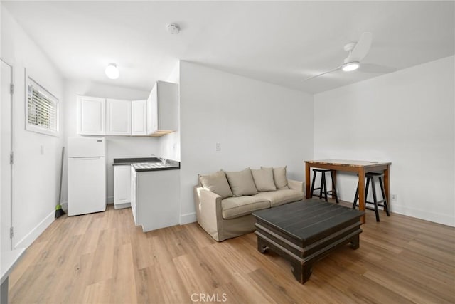 living area featuring light wood-style flooring, baseboards, and ceiling fan