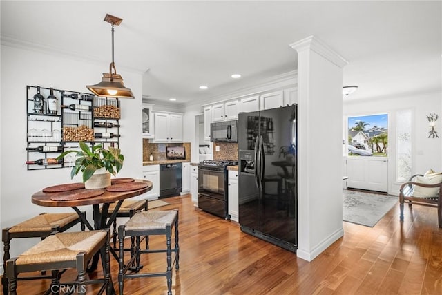 kitchen featuring ornamental molding, black appliances, white cabinets, tasteful backsplash, and light wood-type flooring