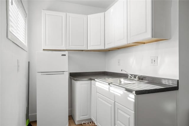 kitchen with dark countertops, white cabinets, freestanding refrigerator, and a sink