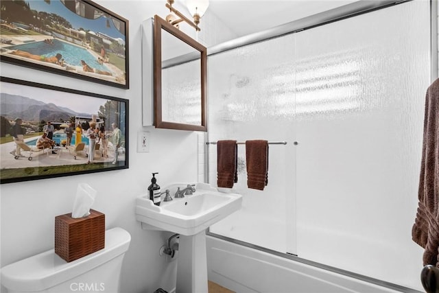 full bathroom featuring toilet, bath / shower combo with glass door, and a sink