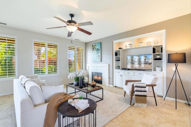 tiled living room with built in features, a wealth of natural light, a tile fireplace, and ceiling fan