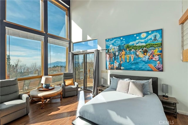 bedroom featuring a towering ceiling, wood-type flooring, and access to exterior