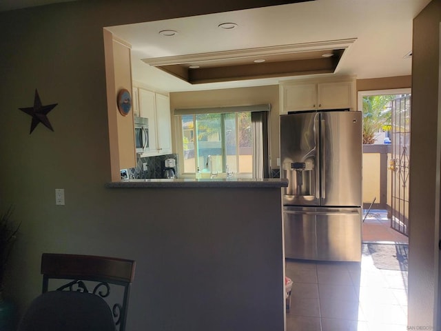 kitchen with a tray ceiling, tasteful backsplash, light tile patterned floors, kitchen peninsula, and stainless steel appliances