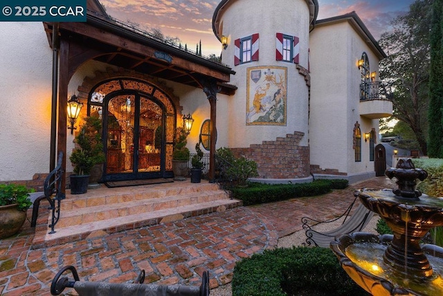 exterior entry at dusk featuring a balcony and french doors