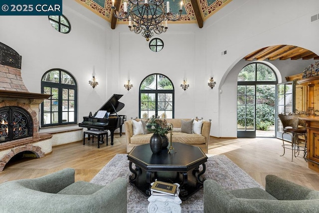 living room featuring a brick fireplace, light wood-type flooring, a notable chandelier, beamed ceiling, and a high ceiling