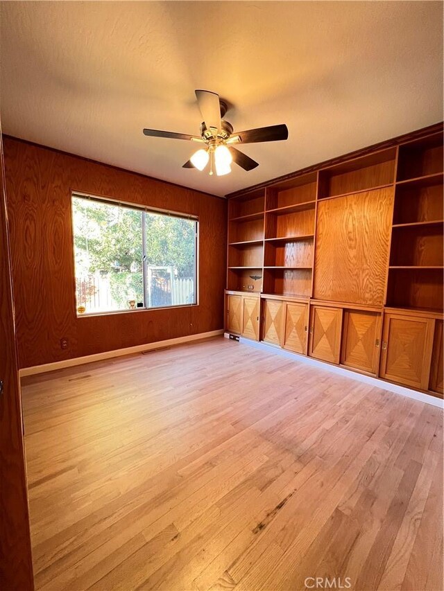 unfurnished room with built in features, wood walls, ceiling fan, and light hardwood / wood-style flooring