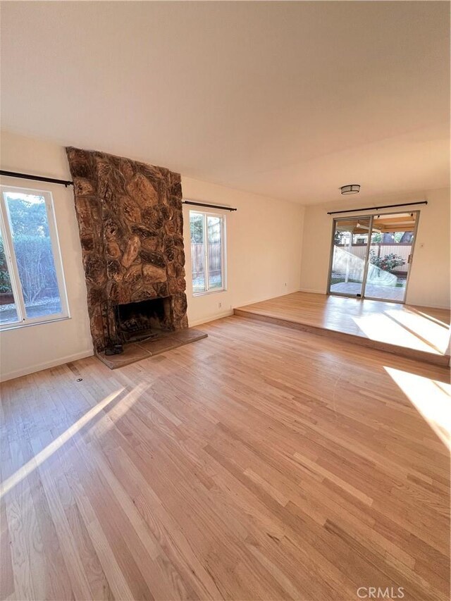 unfurnished living room featuring a healthy amount of sunlight, a stone fireplace, and light hardwood / wood-style flooring