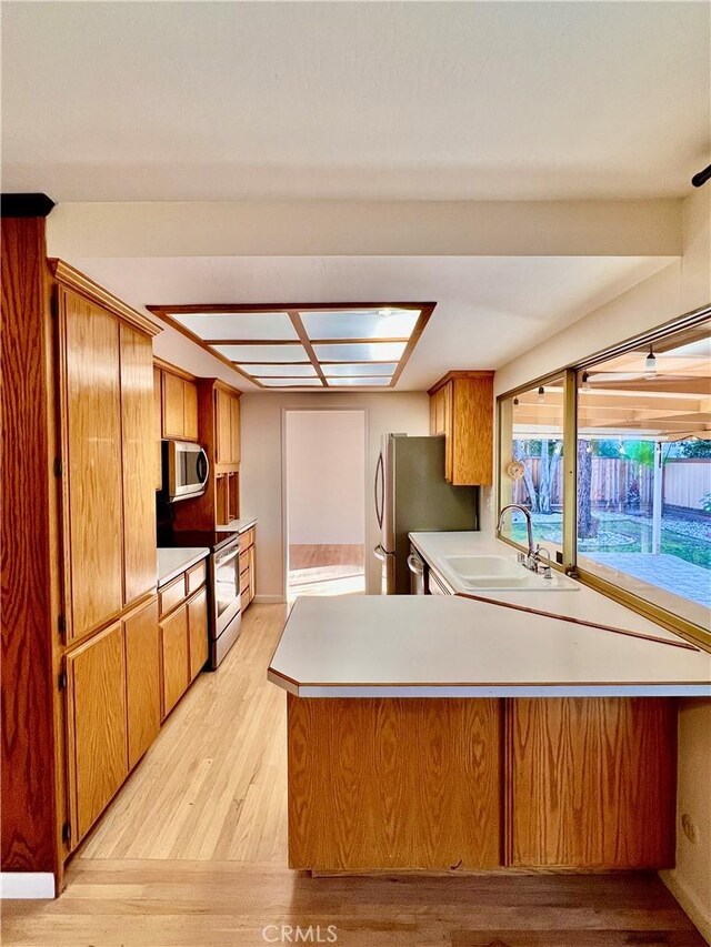 kitchen with sink, stainless steel appliances, kitchen peninsula, and light wood-type flooring