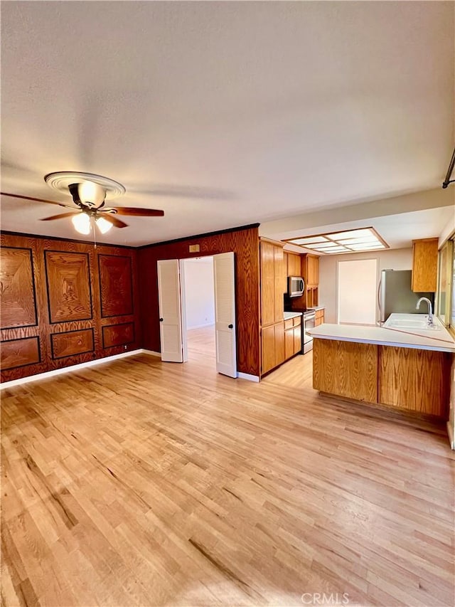 kitchen with sink, light hardwood / wood-style flooring, appliances with stainless steel finishes, kitchen peninsula, and ceiling fan