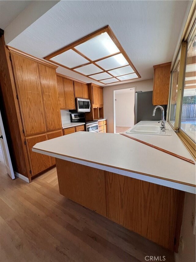 kitchen featuring sink, light wood-type flooring, kitchen peninsula, and appliances with stainless steel finishes