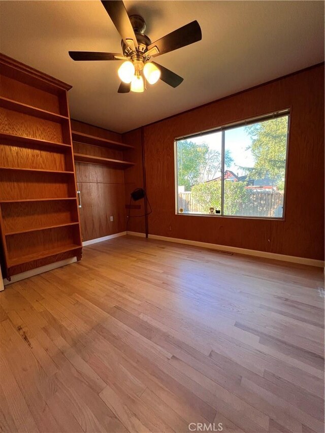 empty room with light hardwood / wood-style floors, ceiling fan, and wood walls