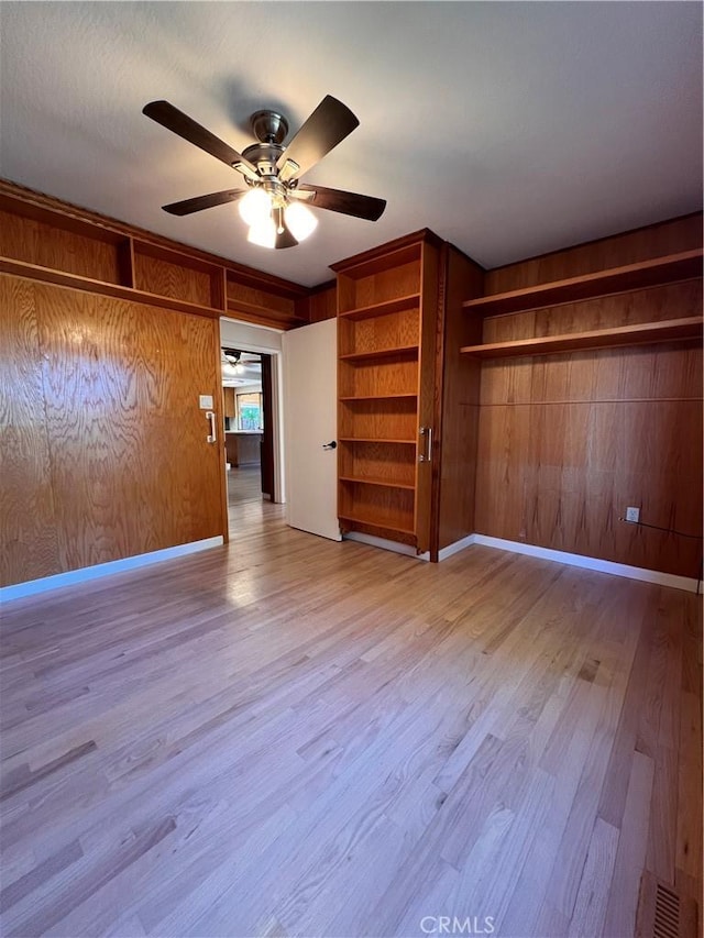 unfurnished bedroom with wooden walls, light hardwood / wood-style floors, and ceiling fan