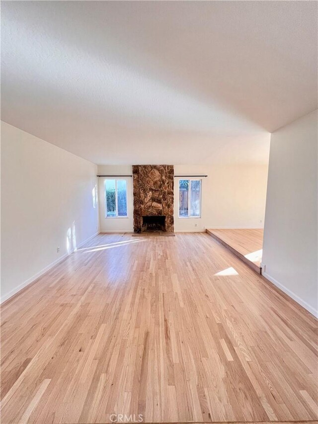 unfurnished living room with a stone fireplace and light wood-type flooring