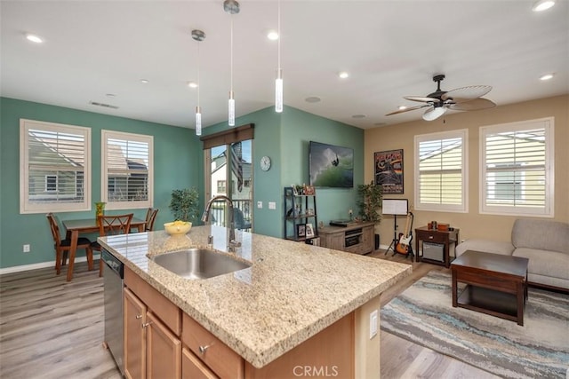 kitchen featuring pendant lighting, an island with sink, sink, stainless steel dishwasher, and light hardwood / wood-style floors