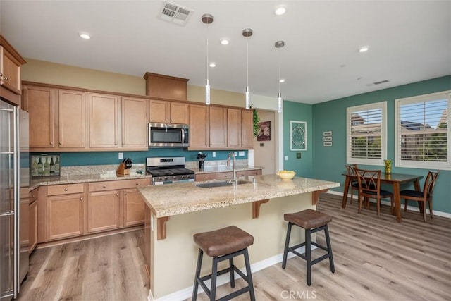 kitchen featuring pendant lighting, sink, stainless steel appliances, light stone countertops, and a center island with sink