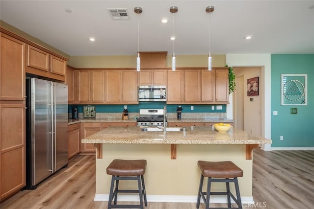 kitchen with appliances with stainless steel finishes, a breakfast bar, a center island with sink, and pendant lighting