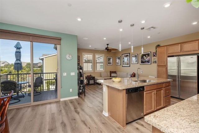 kitchen featuring sink, appliances with stainless steel finishes, hanging light fixtures, a center island with sink, and light wood-type flooring