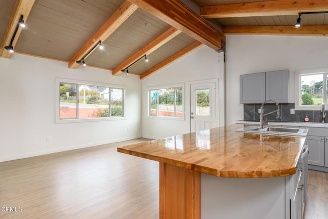 kitchen featuring vaulted ceiling with beams, gray cabinets, a sink, an island with sink, and light wood-type flooring