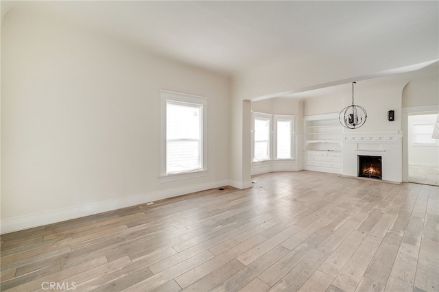 unfurnished living room featuring an inviting chandelier and light hardwood / wood-style floors