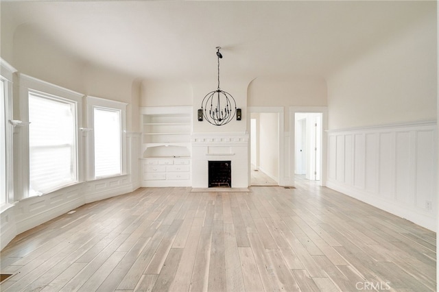 unfurnished living room with built in features, light hardwood / wood-style flooring, and a notable chandelier