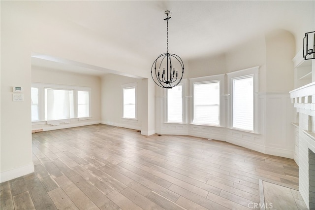 interior space featuring an inviting chandelier, a fireplace, a healthy amount of sunlight, and light wood-type flooring