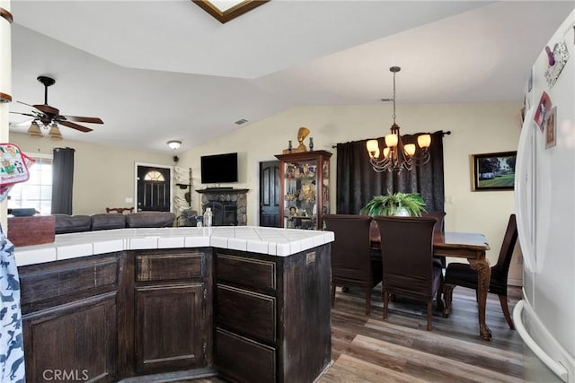 kitchen featuring lofted ceiling, hardwood / wood-style floors, dark brown cabinets, tile countertops, and white fridge