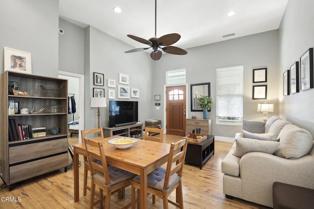 dining space with ceiling fan, a towering ceiling, and light hardwood / wood-style floors