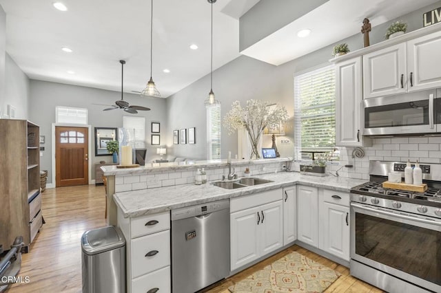 kitchen with appliances with stainless steel finishes, kitchen peninsula, sink, and white cabinets