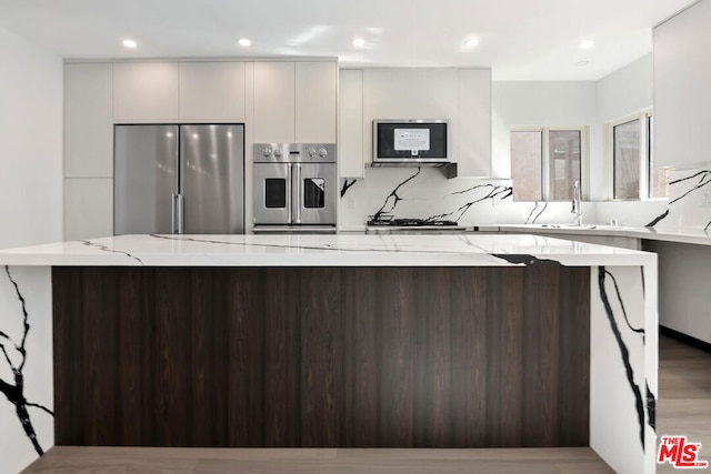 kitchen with stainless steel appliances, a center island, sink, and light stone counters