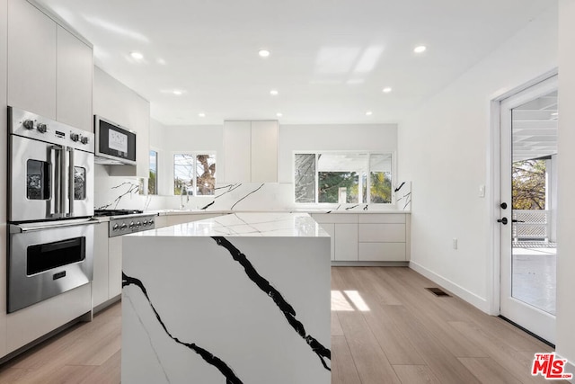 kitchen with white cabinetry, light stone countertops, light hardwood / wood-style floors, and appliances with stainless steel finishes