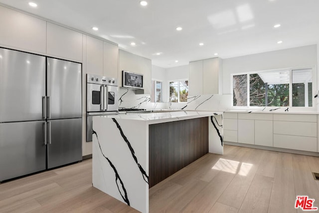 kitchen with a kitchen island, white cabinets, stainless steel appliances, light stone countertops, and light wood-type flooring